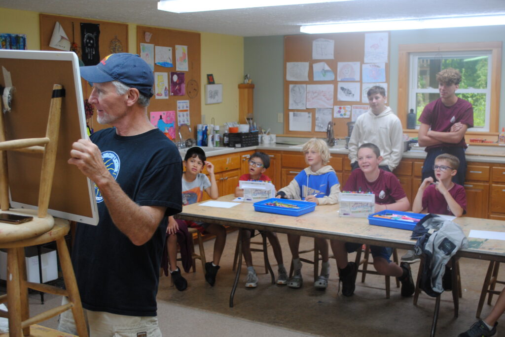 A cartoonist is showing some younger campers how to draw cartoons.