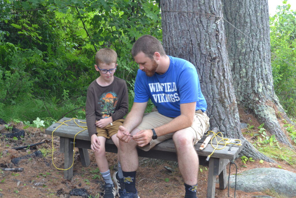 A counselor teaching a camper at campcraft.