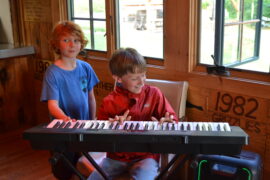 A camper playing the keyboard, with another camper standing behind him.