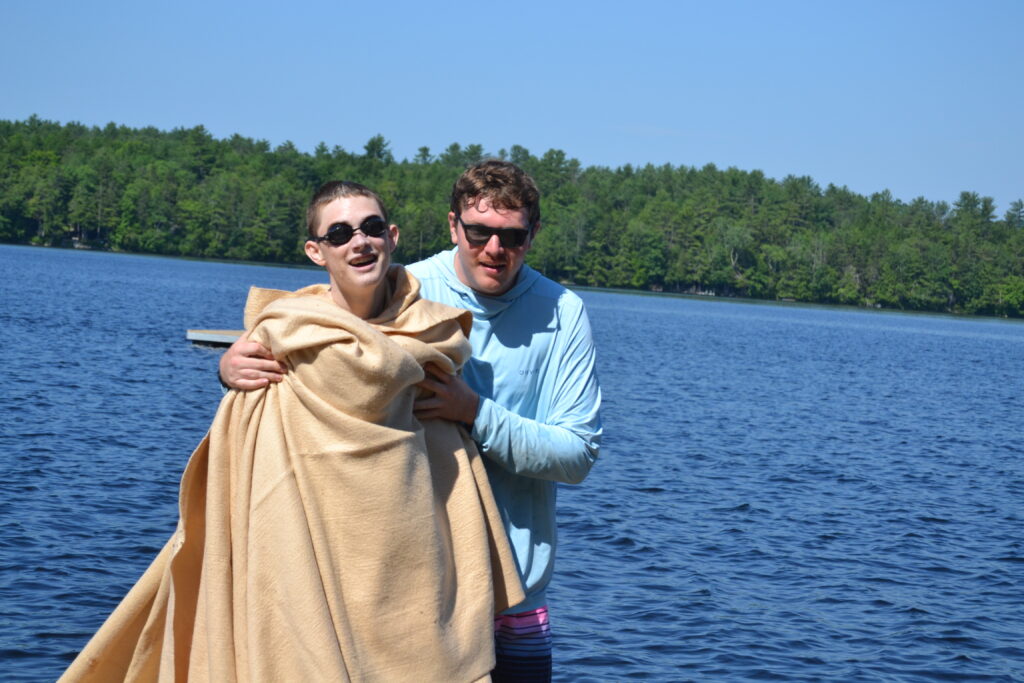 A camper wrapped up in blankets, walking with a counselor, after competing a long distance swim.