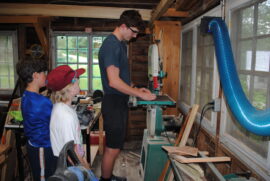 A counselor cutting a piece of wood for campers in the woodshop.